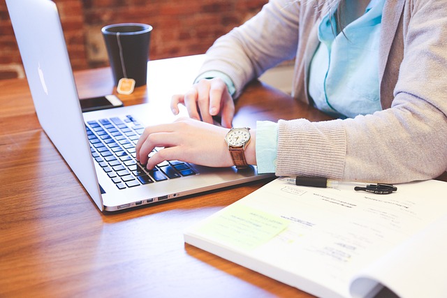 person doing work at computer with book open